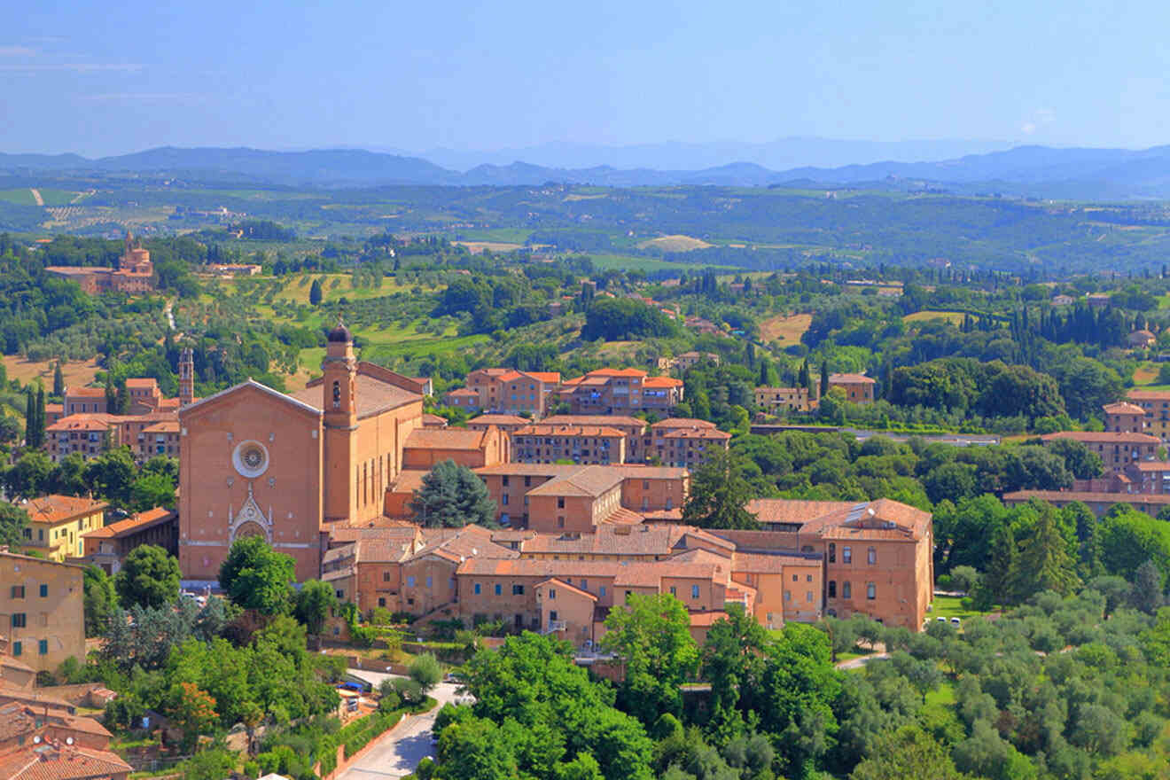 A panoramic view of a picturesque town with historic buildings, a prominent church, and lush green hills in the background under a clear sky.