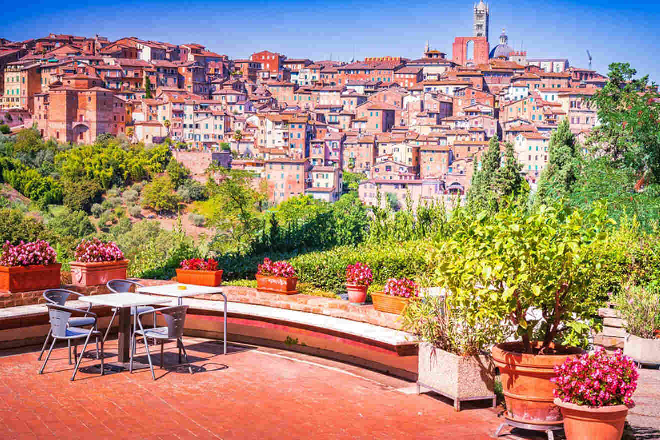 A terrace with potted plants and a table set overlooking a hillside covered with densely packed buildings under a clear blue sky.