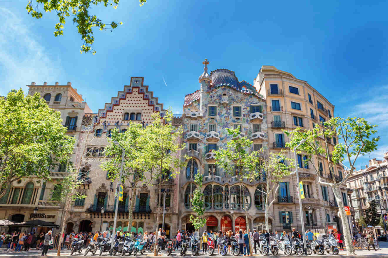 A view of Casa Batlló in Barcelona, Spain, under a clear blue sky, with several people and motorbikes in front of the building.