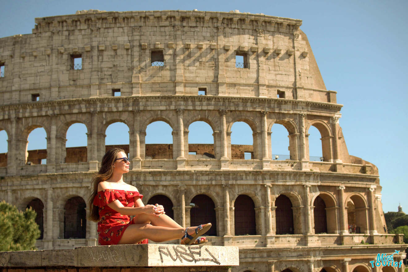 The writer of the post in red dress and sunglasses sits on a ledge near the Colosseum in Rome, enjoying a sunny day.