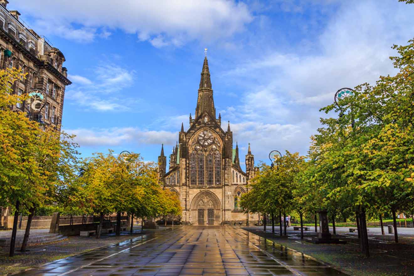 Wide, empty pathway leading to the grand and intricate Gothic architecture of Glasgow Cathedral, with autumnal trees lining the walkway on a clear day