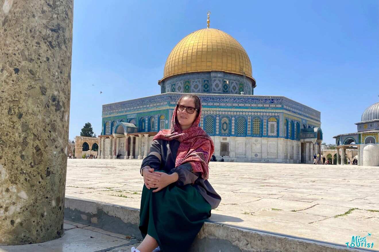 The writer of this post seated in front of the Dome of the Rock, wearing a headscarf, with the iconic golden dome and blue tile work in the background.