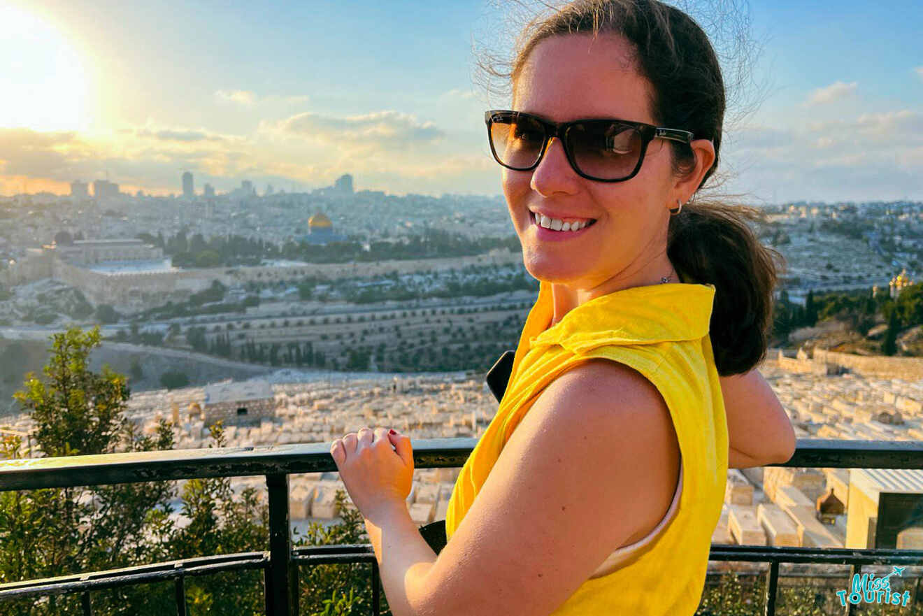 author of the posts wearing sunglasses and a yellow top smiles while standing on a lookout overlooking a vast cityscape with historical buildings and greenery.