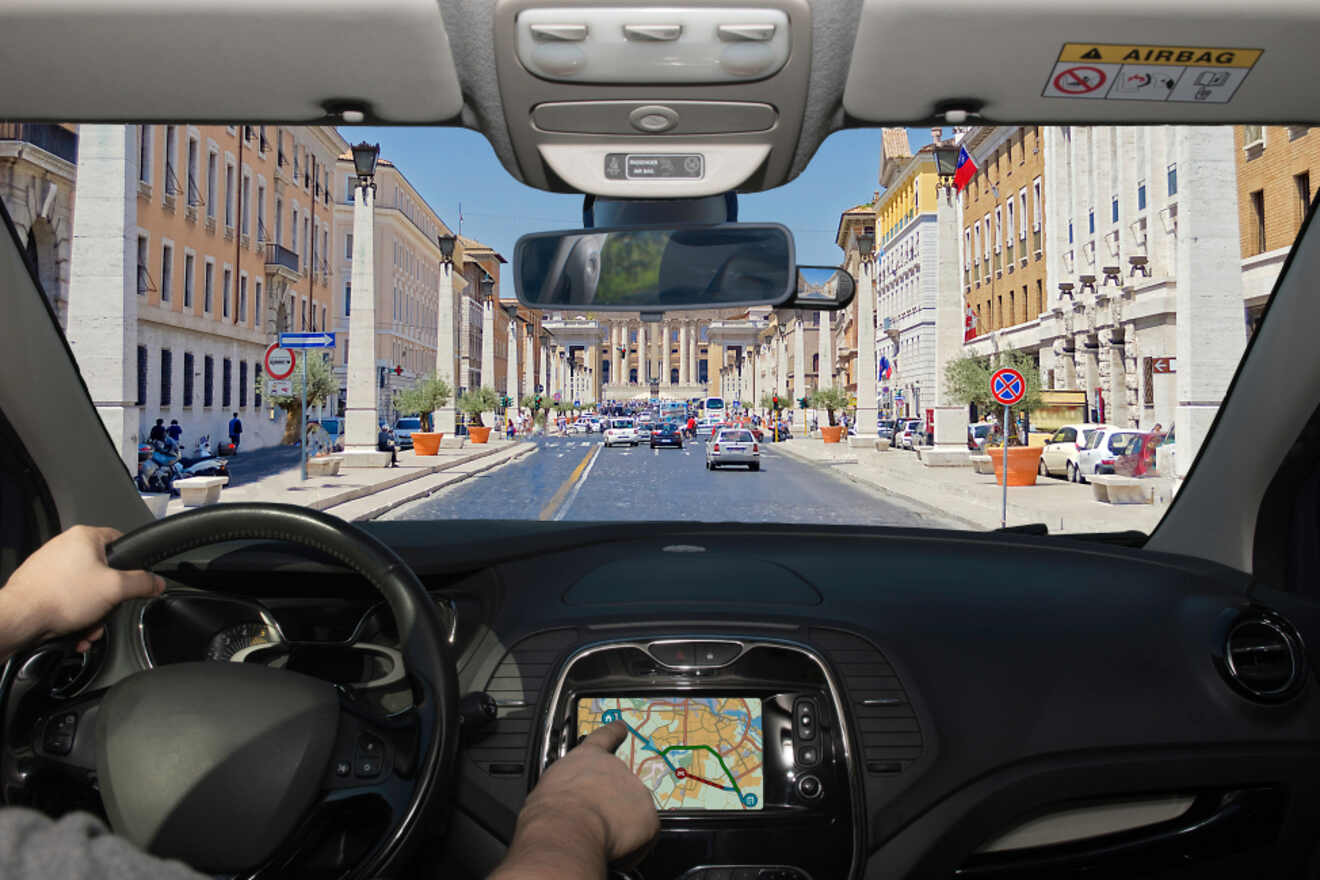 View from inside a car driving through a busy urban street, showing hands on the steering wheel and a GPS on the dashboard.