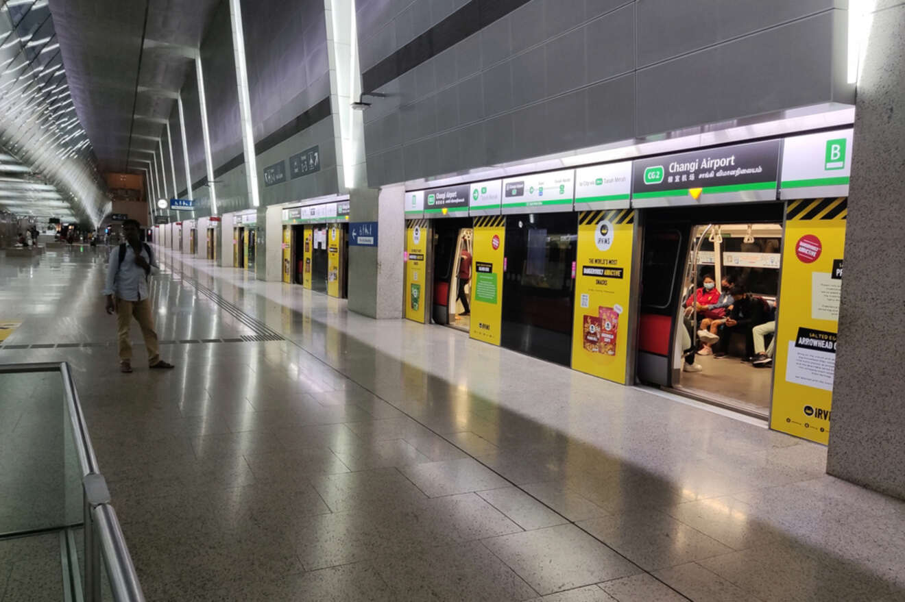 A person walks along an empty subway platform with a train stopped at the station. A few passengers are seated inside the train, and signage indicates it is bound for Changi Airport.