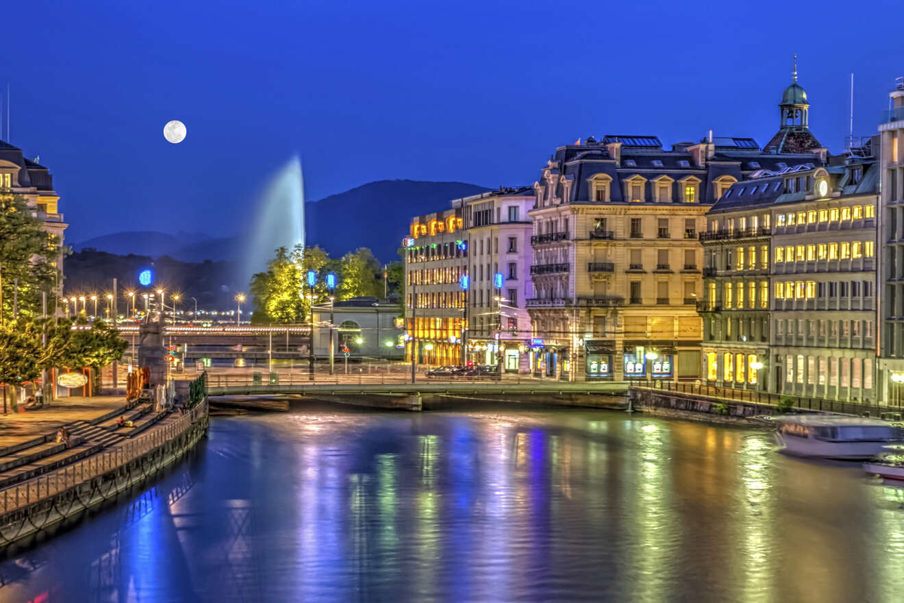 Geneva cityscape at twilight featuring the Jet d'Eau fountain illuminated, with the moon above and the city lights reflecting on the water