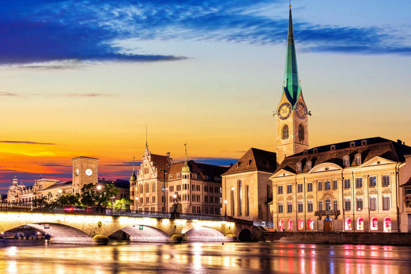 A view of Zurich's old town at sunset, featuring the Fraumünster Church with its tall green spire, historic buildings along the river, and a bridge crossing the Limmat River.