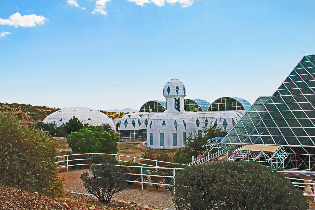 Multiple geodesic domes and pyramidal structures made of glass and metal at Biosphere 2 under a clear blue sky.