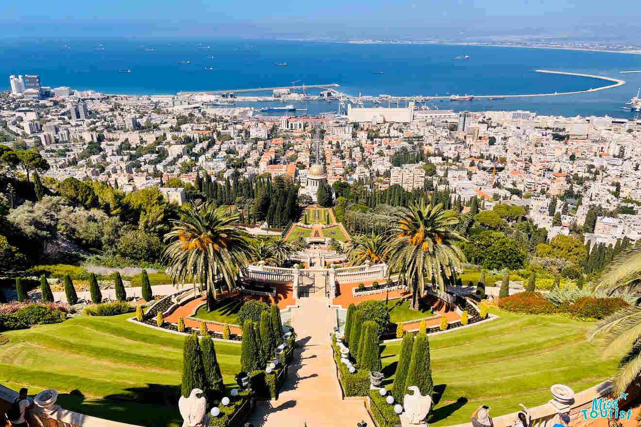 Aerial view of terraced gardens leading to a cityscape with a large bay and port in the background.