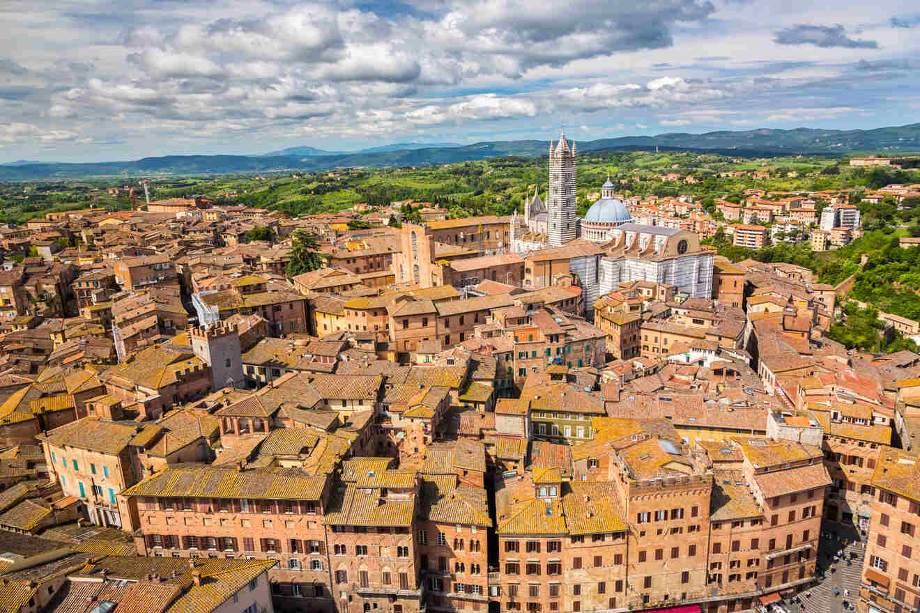 Aerial view of a historic town with a mix of red-tiled roofs, prominent cathedral, and surrounding greenery under a partly cloudy sky.