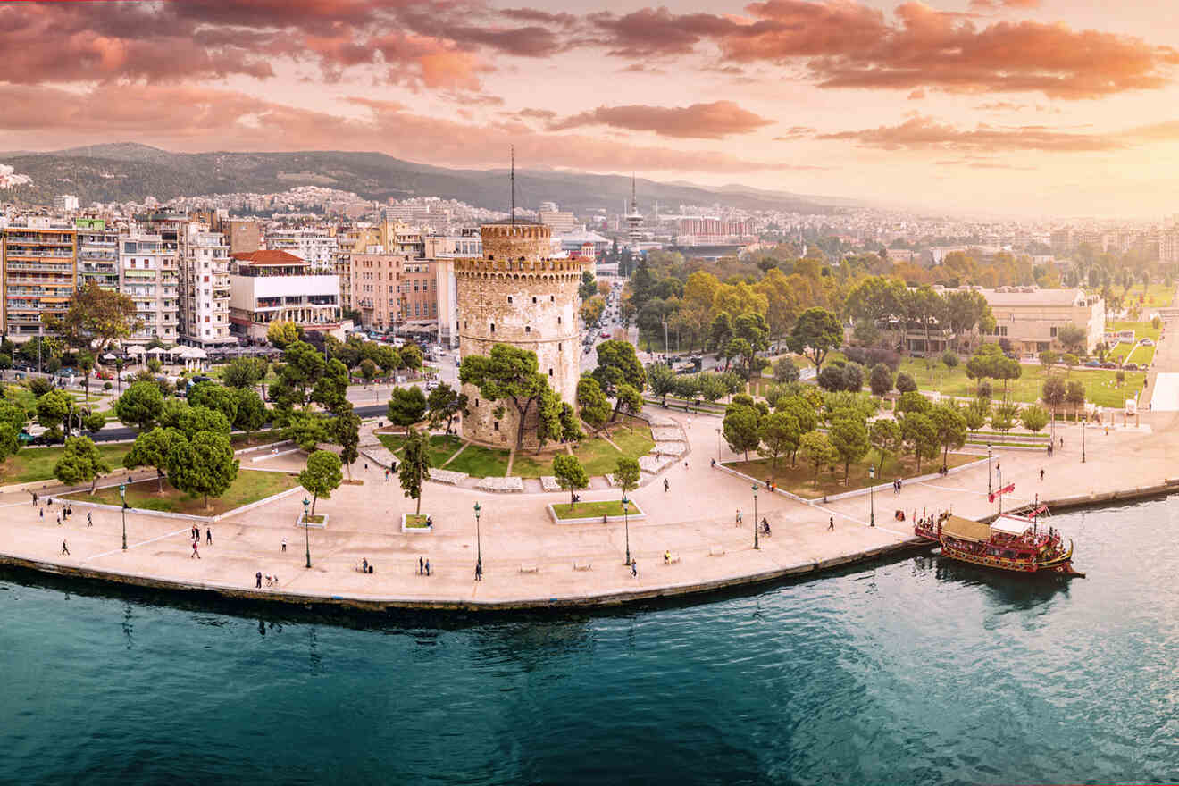 Aerial view of the White Tower in Thessaloniki, Greece, surrounded by green spaces, city buildings, and a body of water with a boat.