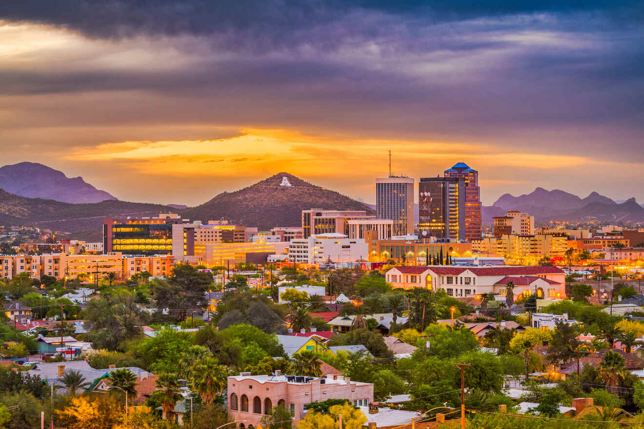 A city skyline at sunset with mountains in the background, showing a mix of tall buildings and residential areas under a colorful sky.